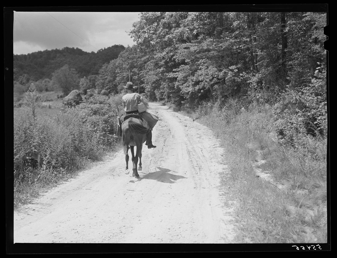 Rural mailman taking packages and saddlebags of letters, which have been transferred from a wagon which cannot go up the bad side roads and creek beds, to the mountain families in 