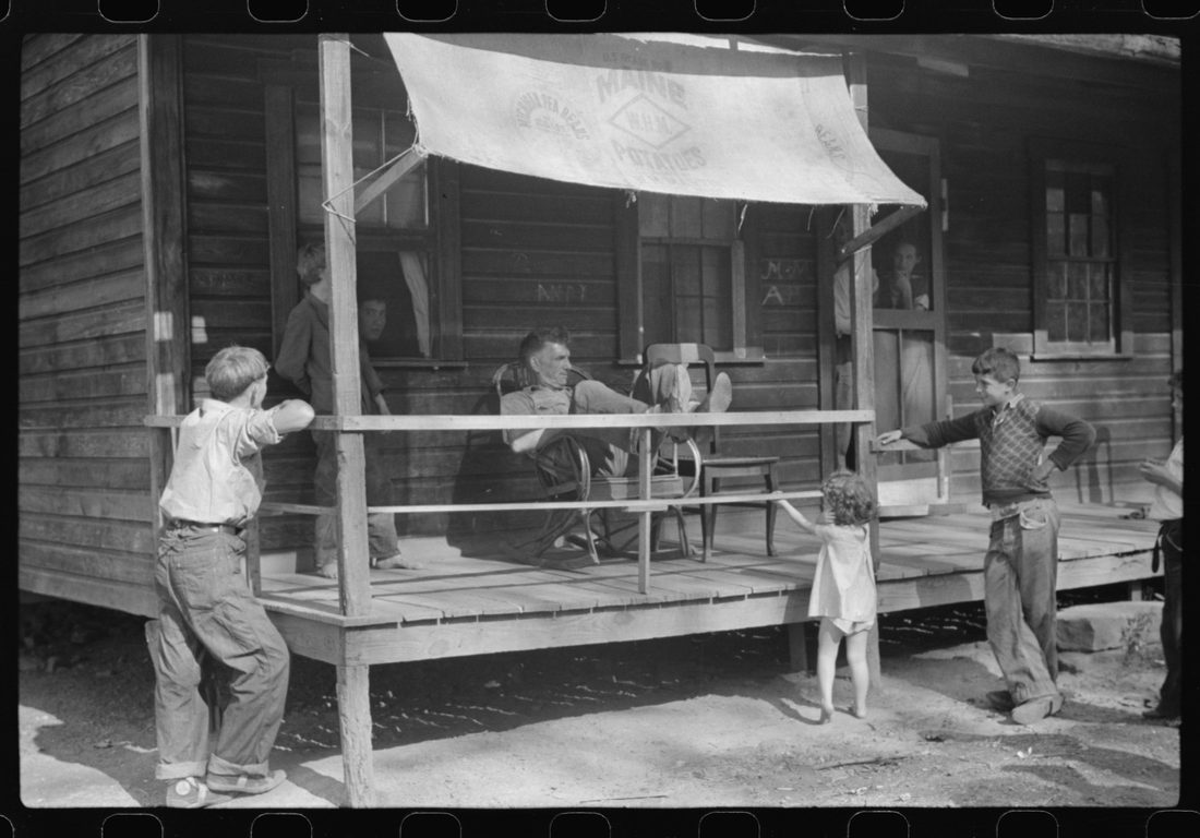 Former coal miner sitting on his front porch. He is the town philosopher. He repairs his home (note railing and potato sack awning). Experiments with an elaborate garden on a hill